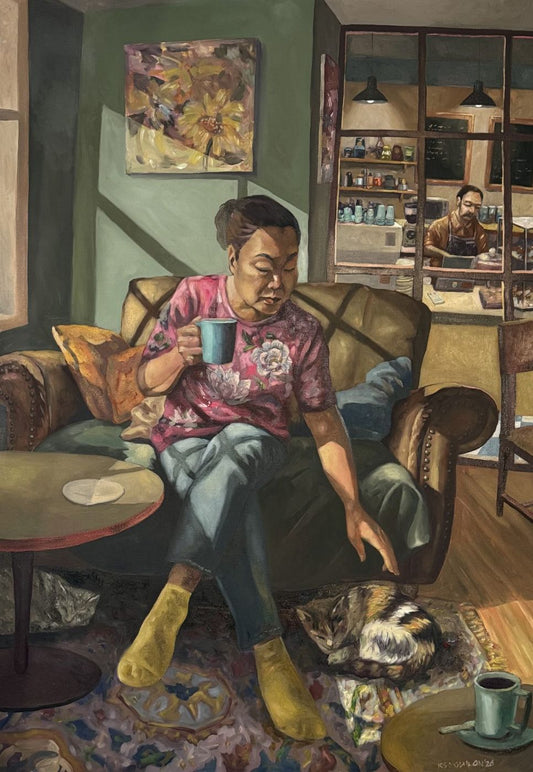 Oil painting of a woman on a leather sofa holding a blue mug and reaching down to a sleeping cat, a café counter behind – Kris Soguilon